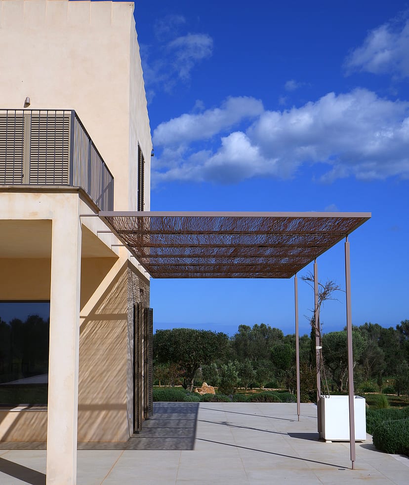 Exterior terrace of a Mallorcan finca with a metal laser-cut pergola casting intricate shadows on the stone floor.