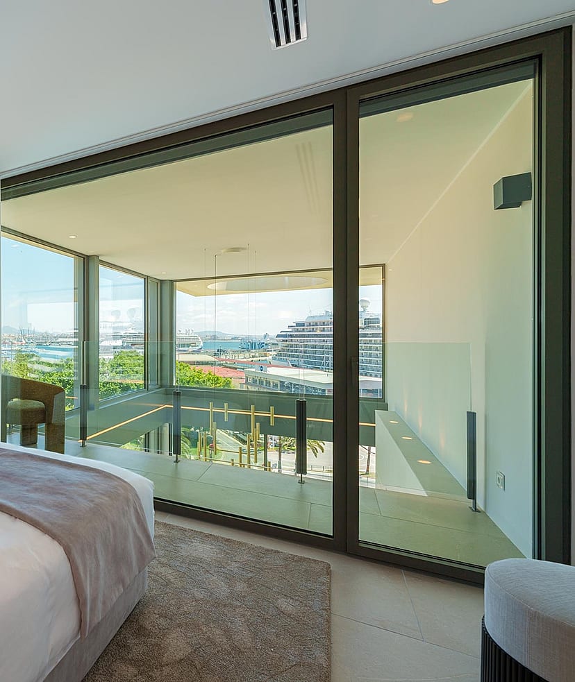 Dormitorio moderno con cama grande, decoración neutra y ventanales correderos con salida a la terraza.
