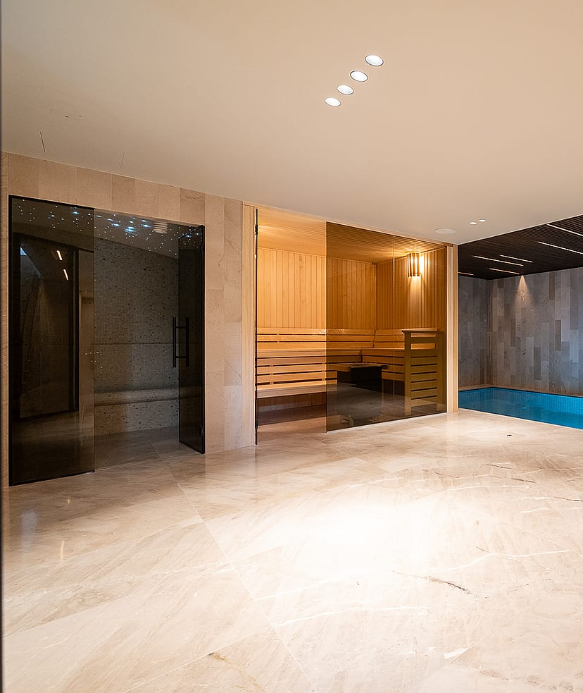 Indoor spa area featuring a tiled lap pool, sauna with glass door, polished stone flooring, and recessed ceiling lighting.