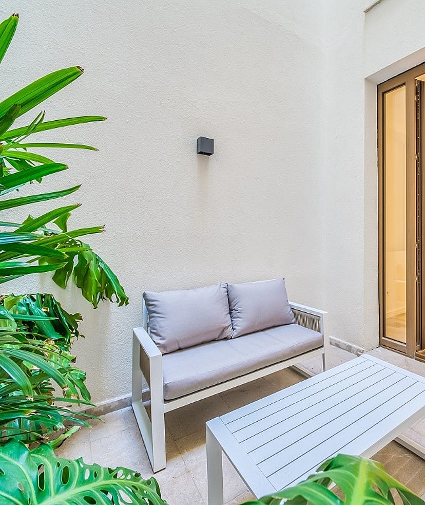 A small outdoor terrace with a two-seater sofa and coffee table next to large glass doors leading into an interior room.
