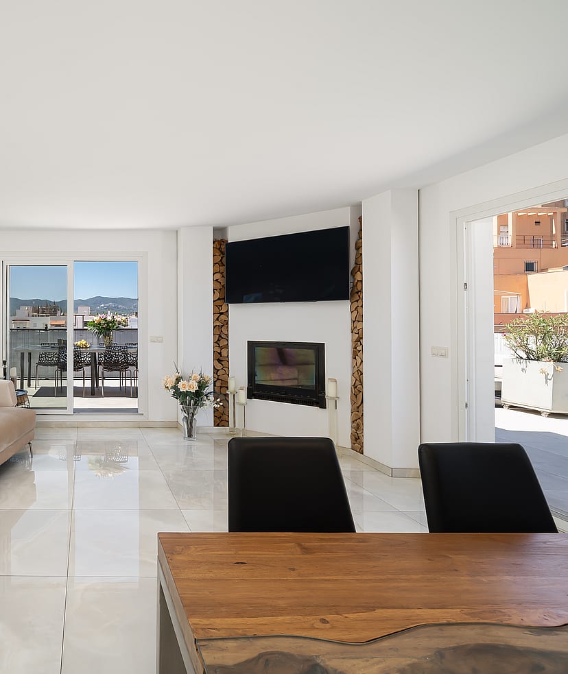 A bright, spacious living room with polished white floors, a long beige sofa, floor-to-ceiling mirrored walls, and a contemporary fireplace.