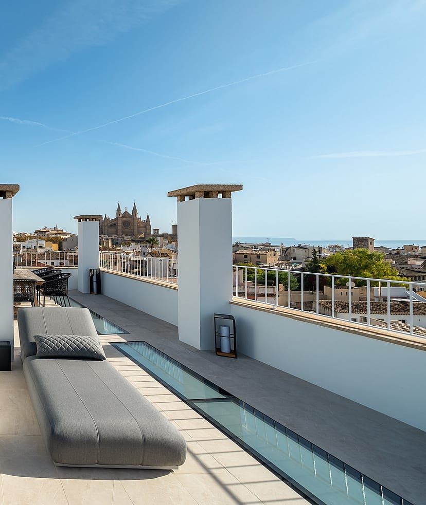 Sun-drenched rooftop terrace with grey loungers, stone flooring, and panoramic views of Palma's historic skyline.