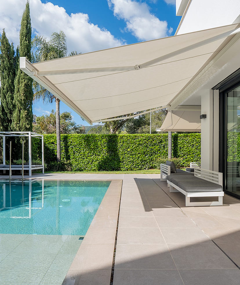 Heated saltwater swimming pool with sun loungers, retractable awning and tall hedge screening.