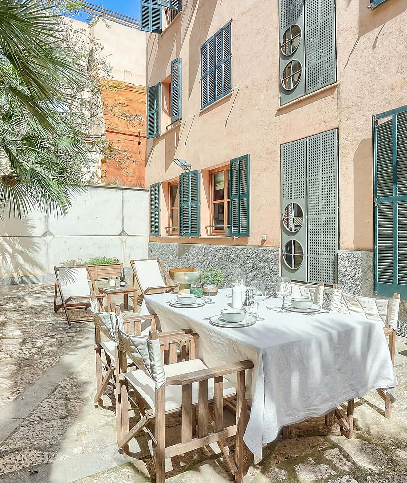 Outdoor terrace in a historic Old Town building with a dining table, folding wooden chairs, and green shutters.