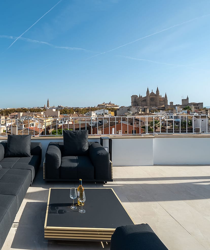 Modern black lounge furniture on a sun-drenched rooftop terrace overlooking Palma Old Town and the Cathedral.