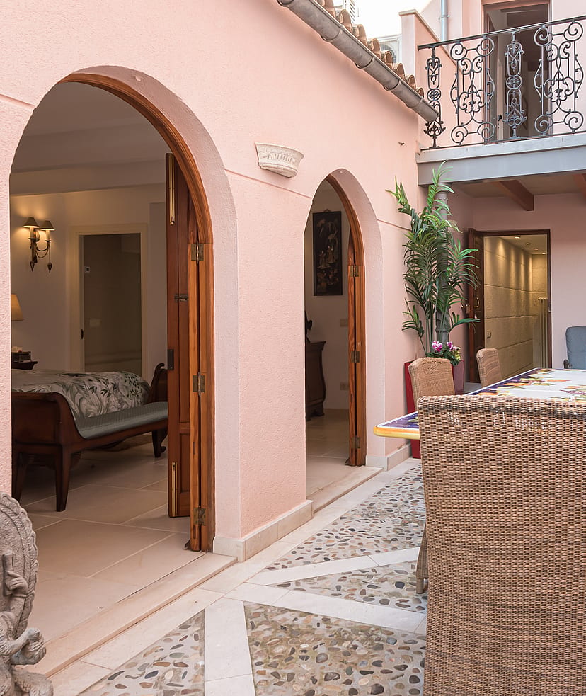 Pink-walled courtyard patio with a tiled dining table, potted plants and arched doorways