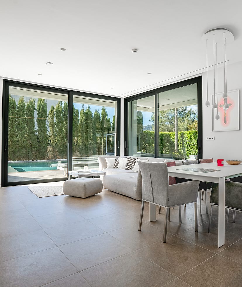 Open-plan living and dining room with corner sliding glass walls opening to the pool terrace and garden.