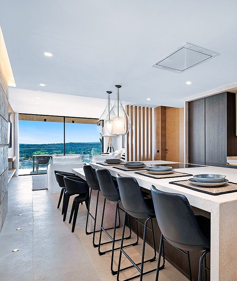Modern kitchen with large white stone island, dark bar stools, and sliding glass doors opening to a mountain terrace.