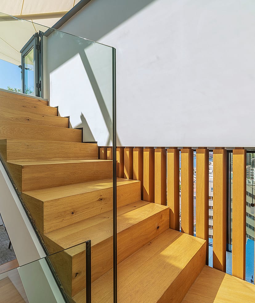 A modern interior staircase featuring solid oak treads and vertical timber slat railings, complemented by a transparent glass balustrade.