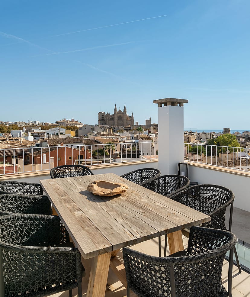 Rooftop terrace with wooden dining table and black chairs overlooking Palma Cathedral and the Mediterranean sea.