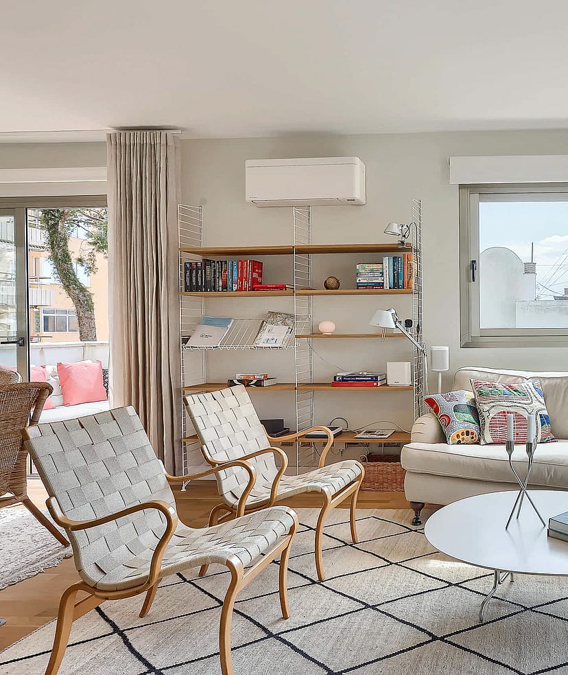 Bright living room featuring a neutral sofa, patterned armchairs, metal shelving, and a large window leading to a terrace.