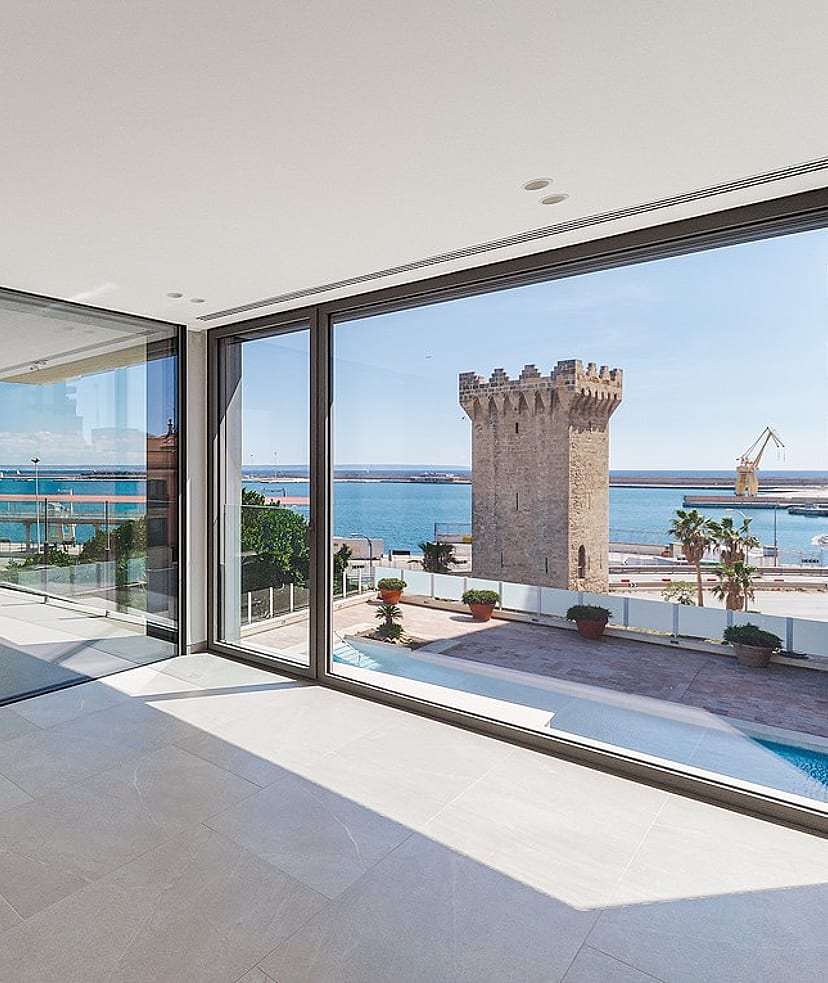 Light-filled corner living space with floor-to-ceiling glass on two elevations framing Palma harbour and open sea