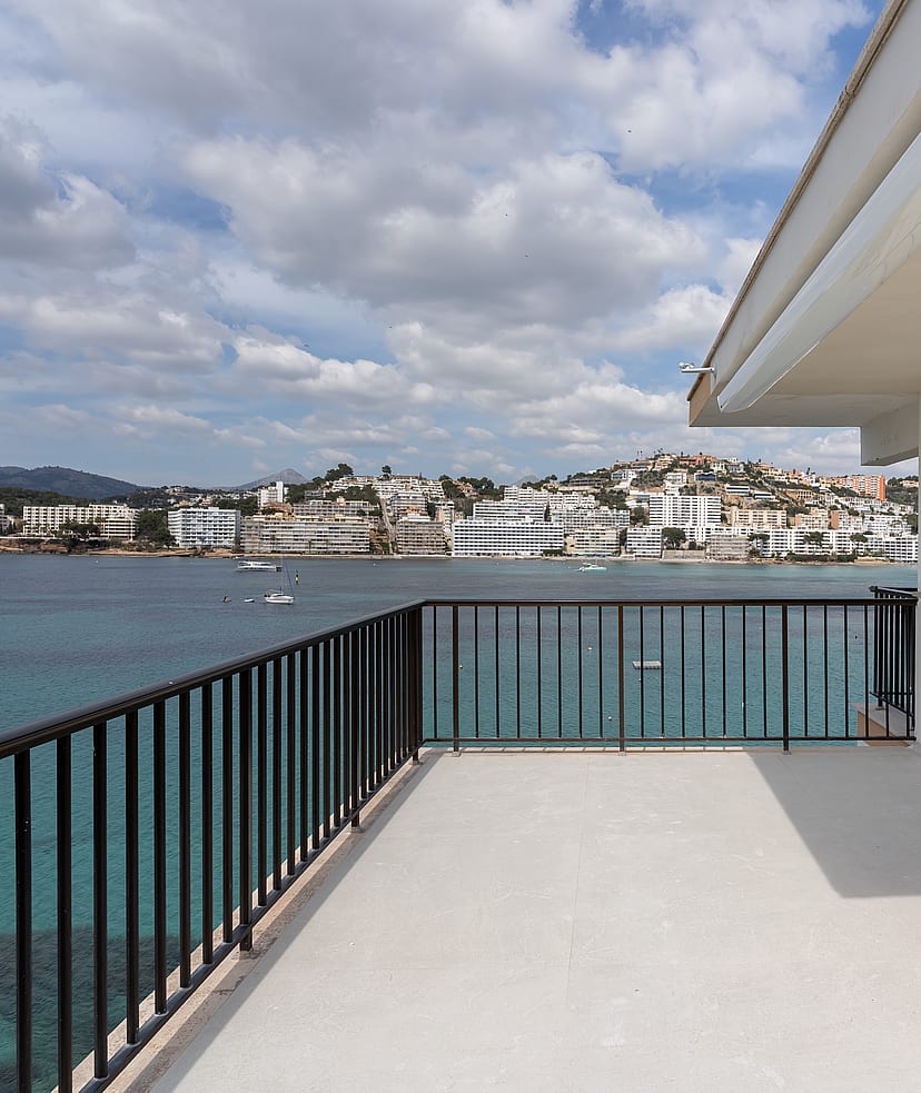 A spacious grey-tiled terrace with black metal railings faces a bay filled with boats under a cloudy sky.