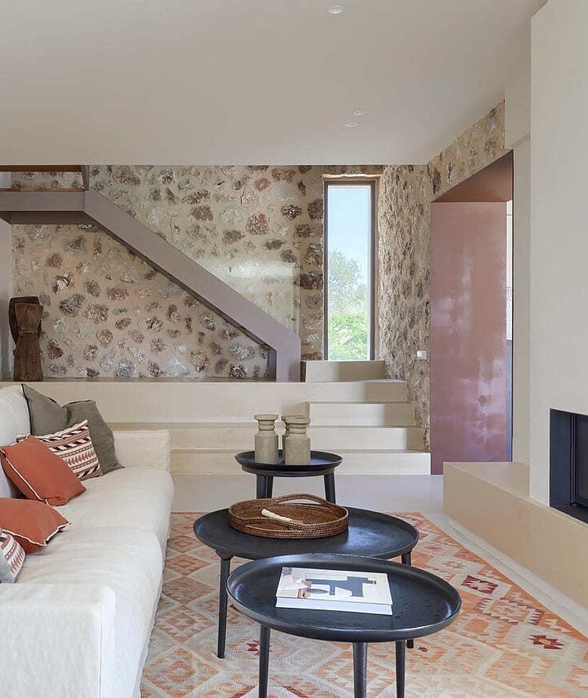 Interior view of a living room featuring a cream sofa, stone accent wall, inset fireplace, and floating staircase steps.
