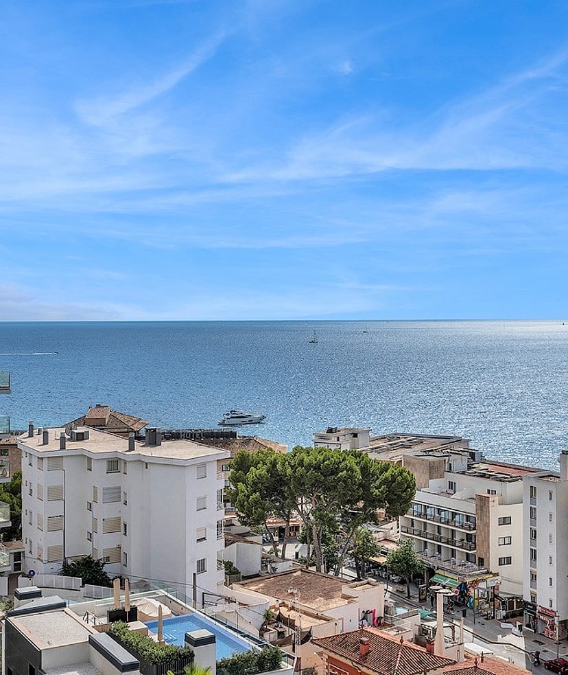 Wide-angle view looking over the Cala Mayor coastline towards the open sea with white buildings and blue water.