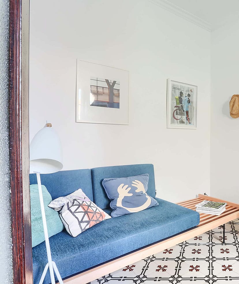 A small living space featuring a blue upholstered daybed, patterned floor tiles, a chrome side table, and a modern chair.