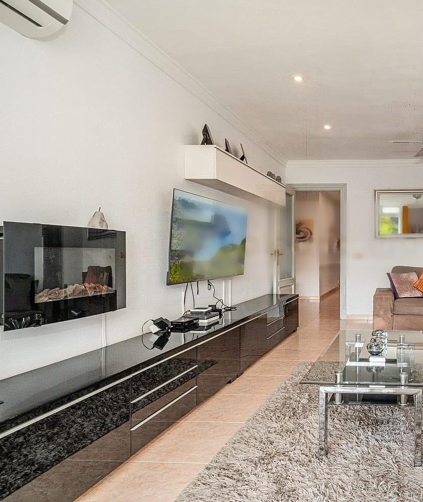Living room featuring a brown sofa, glass coffee table, wall-mounted electric fireplace, and dark glossy media console.