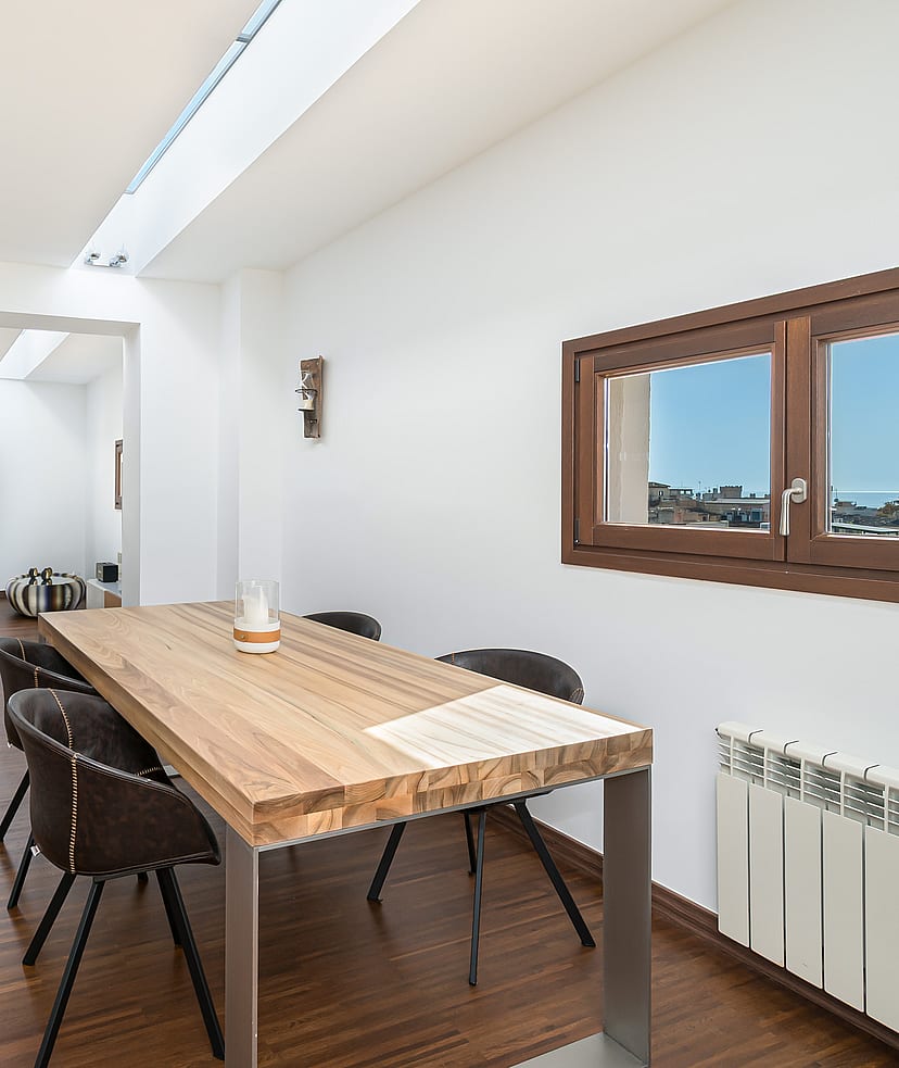 Modern dining area with oak table, dark chairs, and a long linear skylight over dark wood floors.