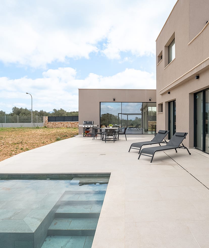 Wide view of a modern villa terrace featuring a rectangular swimming pool, sun loungers, and large sliding glass doors.