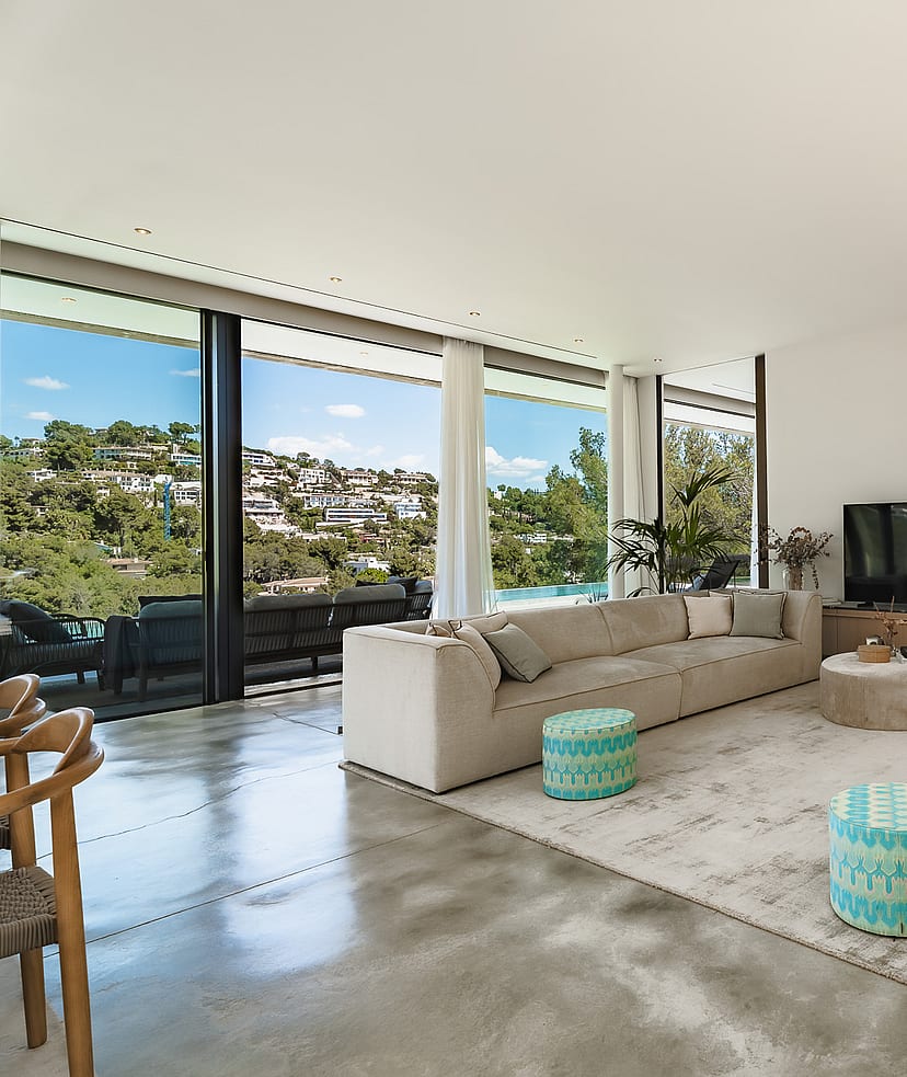 Modern living room with polished concrete floors, modular sofas, and full-height glass doors overlooking the hills.