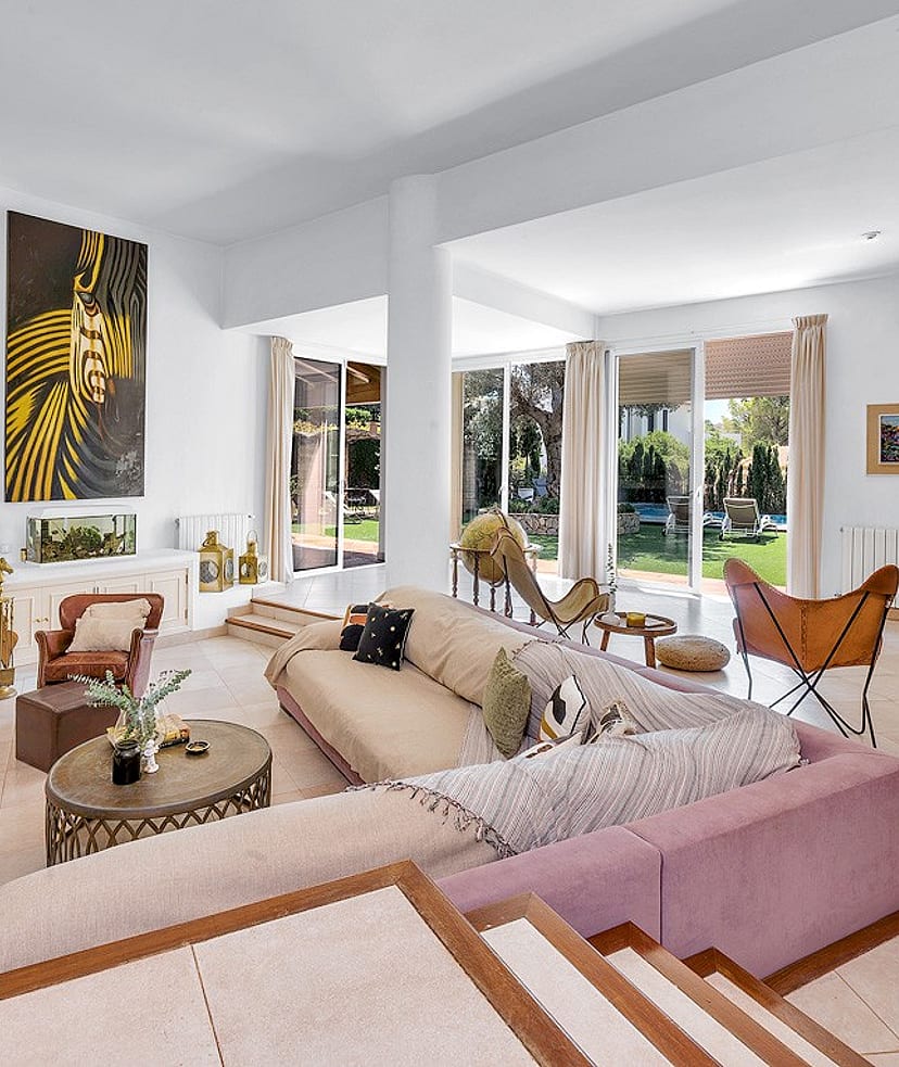A bright, open-plan living room with a large corner sofa, a fireplace, and glass doors leading to an outdoor garden area.