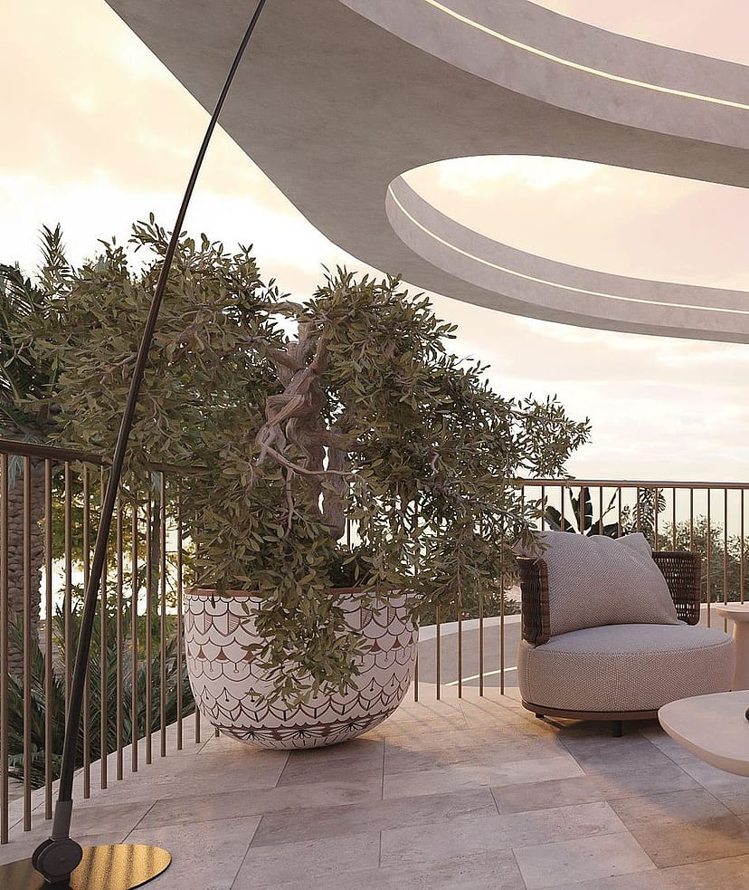 A modern curved terrace overlooking the sea at sunset, featuring stone flooring, outdoor seating, and a large potted plant.