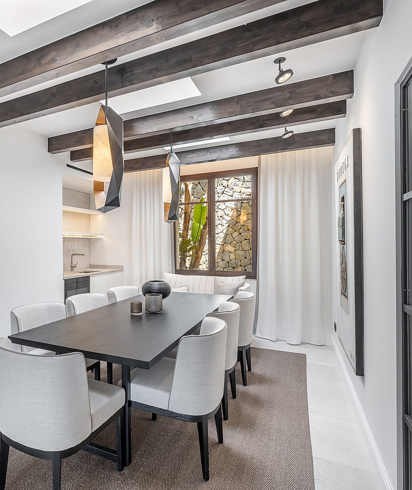 Modern dining room featuring a dark wood table, grey upholstered chairs, exposed ceiling beams, and integrated skylights.