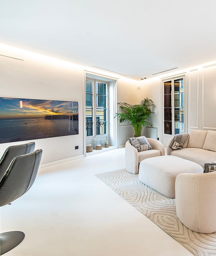 A bright, modern living room featuring cream-colored textured armchairs, a large sofa, and white walls with vertical paneling.