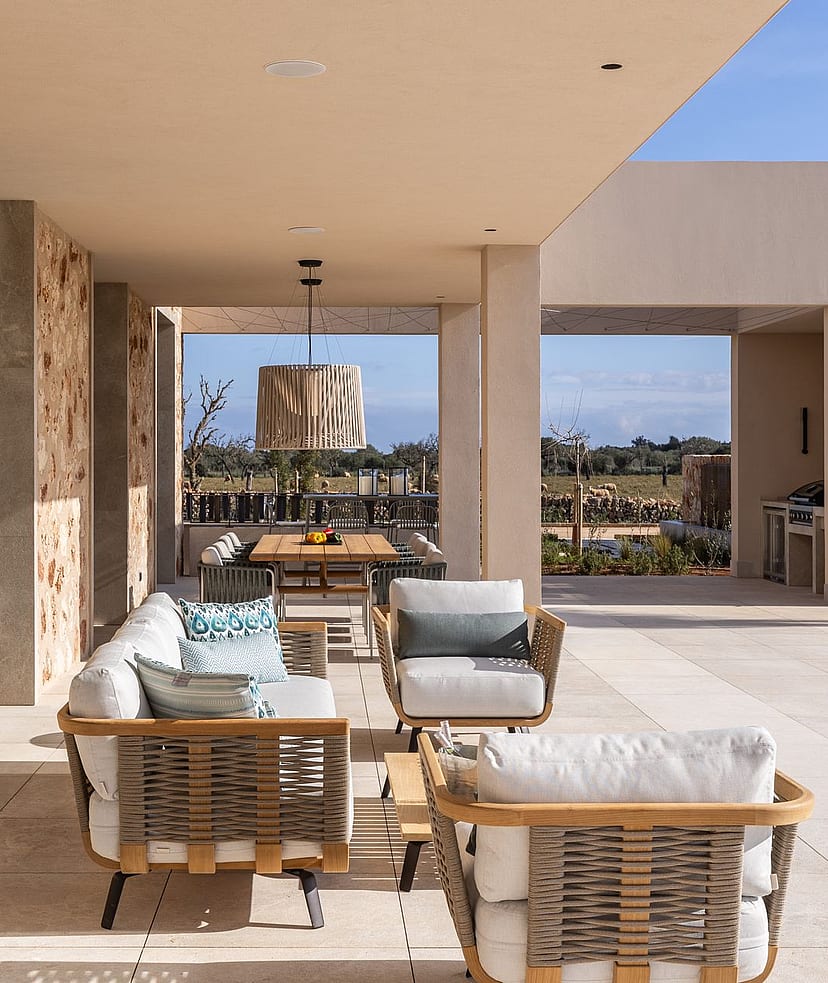 A spacious covered terrace with stone walls, outdoor lounge seating, and a dining area, overlooking a distant mountain landscape.