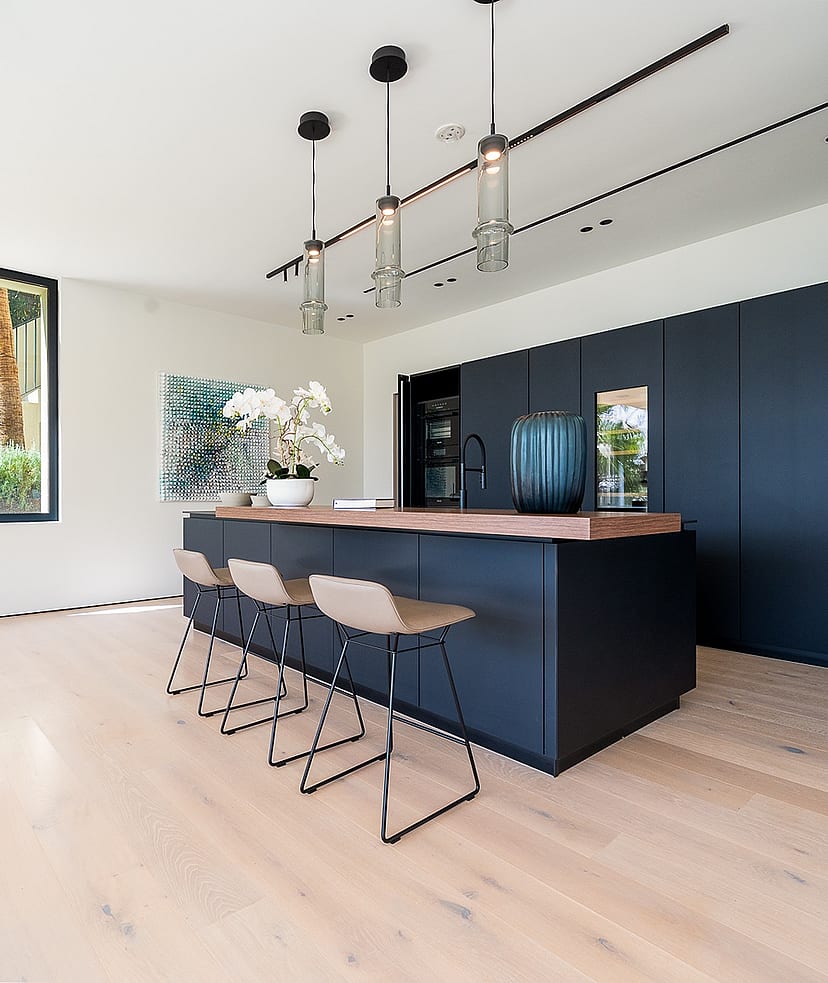 Modern open-plan kitchen featuring a dark matte island, light oak hardwood floors, and three pendant lights in Son Vida.