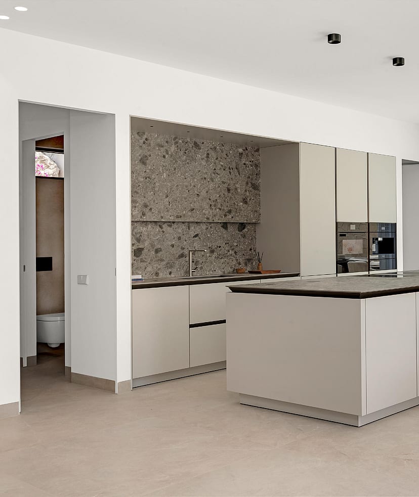 Handleless island kitchen with dark stone worktop, terrazzo-effect splashback and garden views