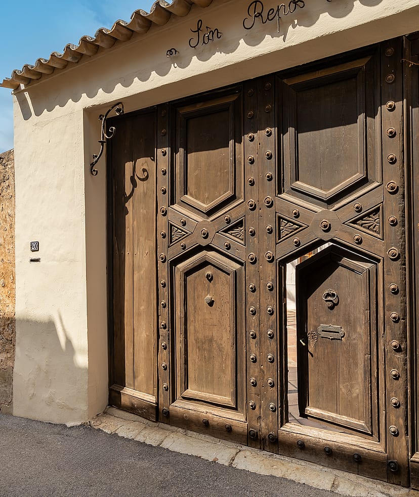 Heavy dark wood gate with iron studs and an inset pedestrian door set into a stone wall under tiled eaves.