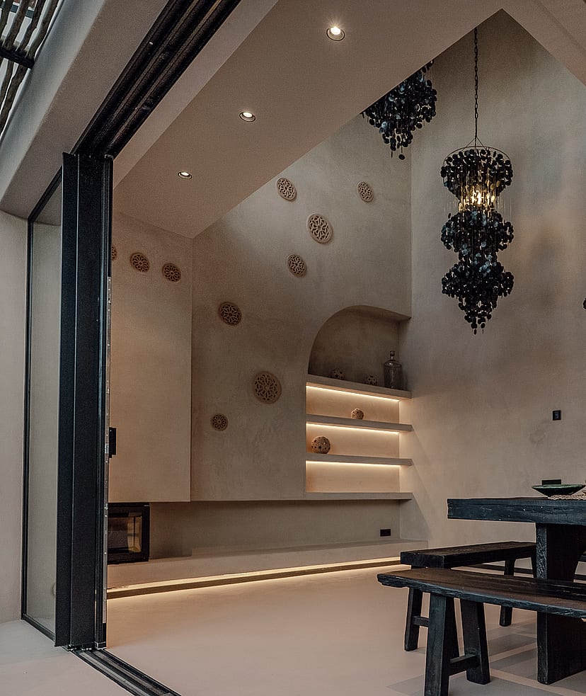 Dining area featuring a dark wooden farmhouse table and benches, sculptural black pendant lights, and arched wall niches with soft integrated illumination.