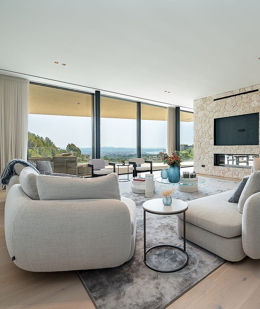 Contemporary living room with light oak floors, a textured stone fireplace wall, and floor-to-ceiling windows facing the sea.