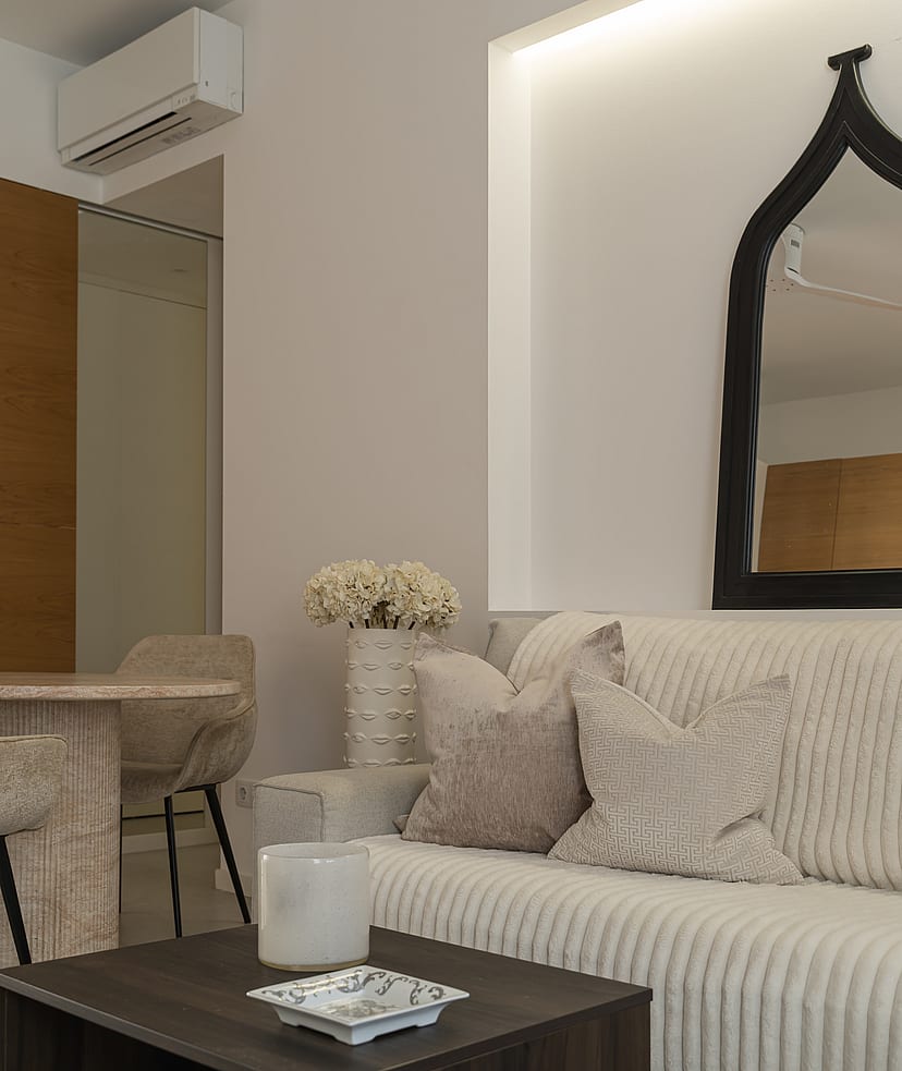 A modern living area featuring a ribbed beige sofa, dark wood coffee table, and an arched black-framed wall mirror.