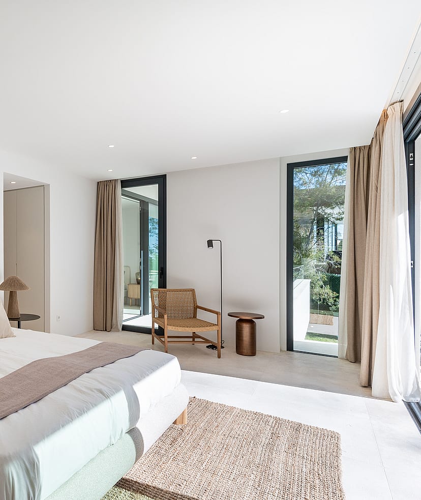 Serene master bedroom with neutral linen bedding, rattan accent chair and floor-to-ceiling sliding doors to a private terrace with pine tree views