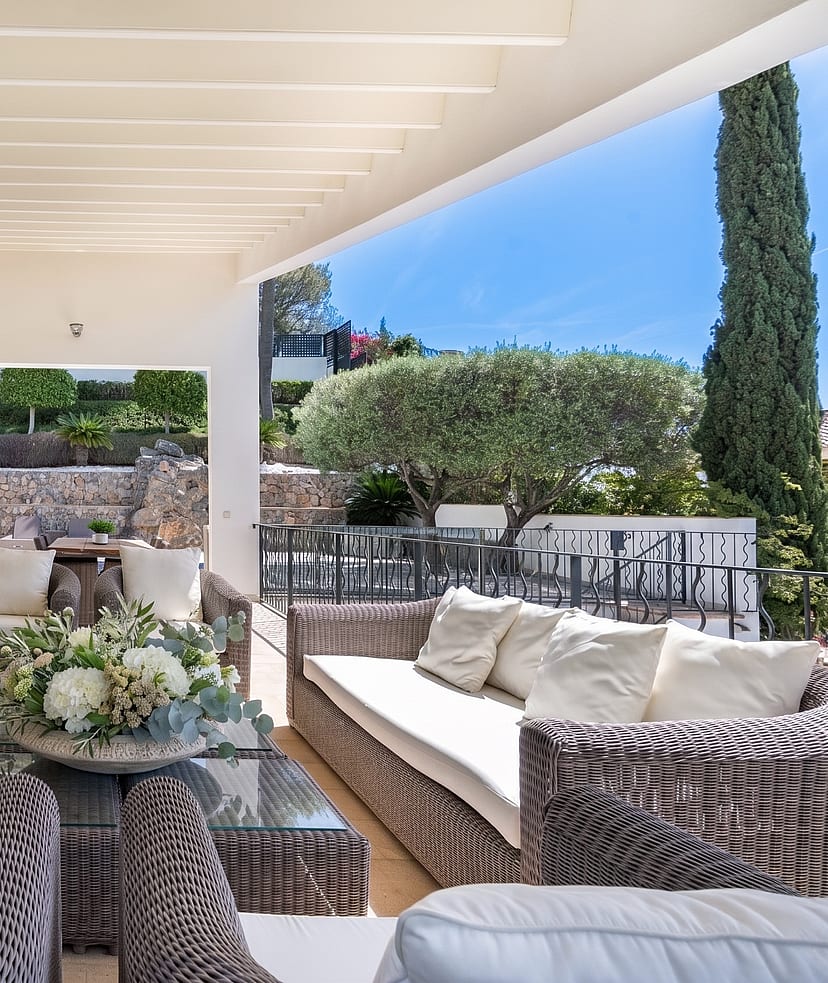 Covered outdoor terrace with rattan sofa set and far-reaching sea and mountain views at a villa in Son Vida, Mallorca
