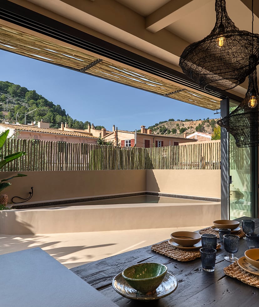 Dining room with large sliding doors opening to an outdoor terrace with a pool, overlooking a hillside.
