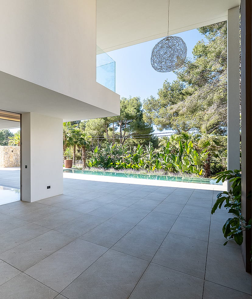 Interior view of a contemporary living area with large floor-to-ceiling glass doors opening onto a sunlit pool terrace.