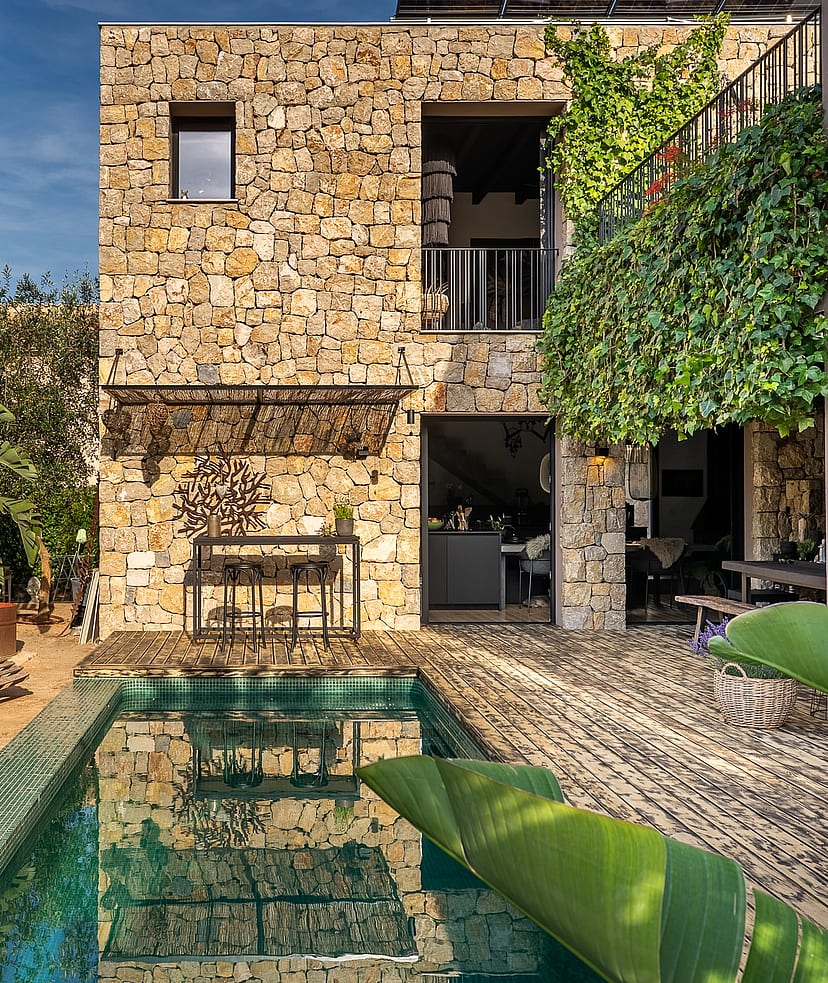 Exterior view of a stone-clad villa in Genova featuring a rectangular swimming pool, lush greenery, and climbing vines.