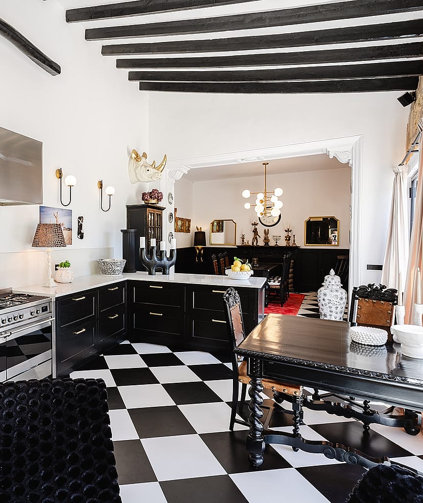 Kitchen features black and white checkered tile floors, black cabinets, a stainless steel range, and exposed dark wood beams.