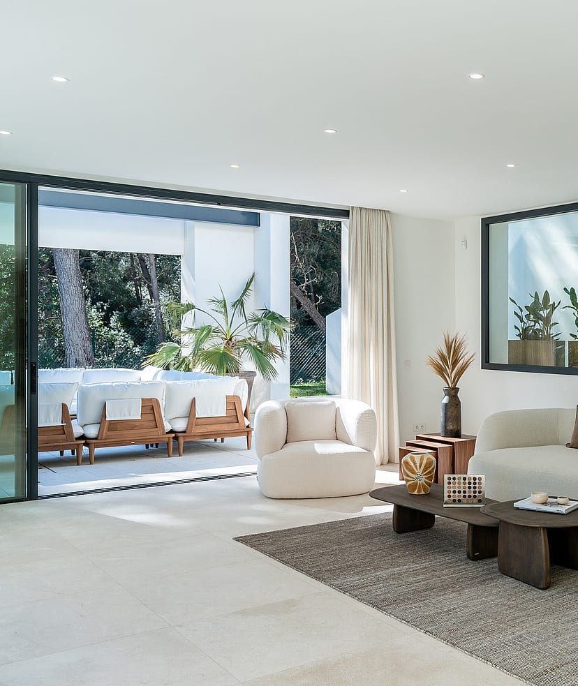 Spacious open-plan living room with bouclé sofas, stone flooring and floor-to-ceiling sliding doors opening to the pool terrace