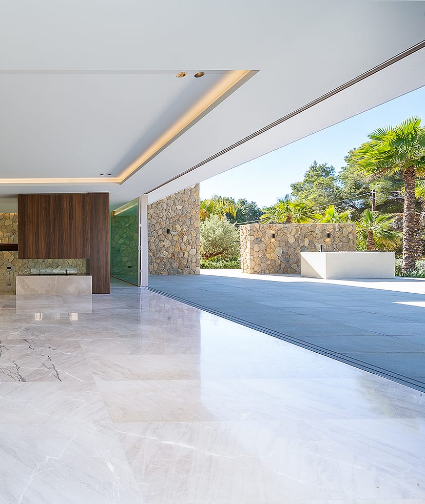 Modern open-plan kitchen with a stone island, floor-to-ceiling sliding glass doors, and polished marble flooring.