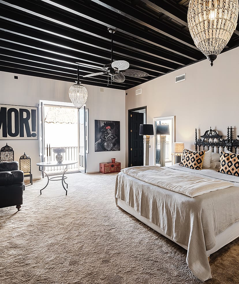 A spacious master bedroom in a Sencelles townhouse featuring a black exposed beam ceiling, a wrought iron bed, and neutral walls.