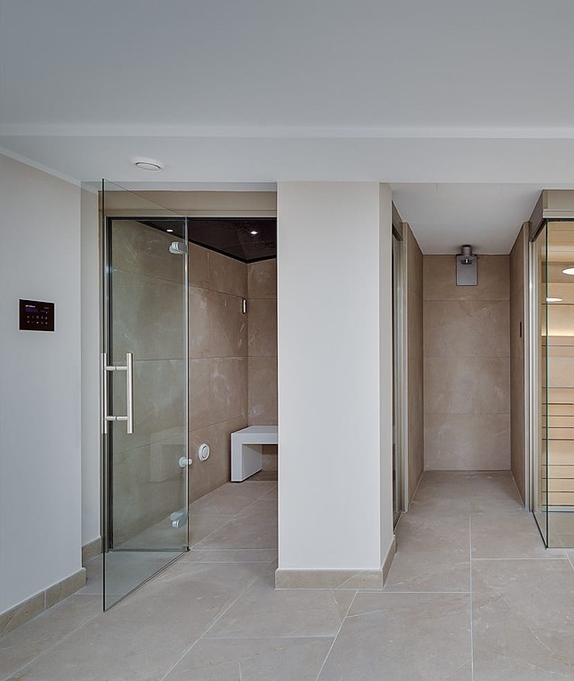 Glass-enclosed steam room with marble-effect tiles alongside a Finnish sauna with cedar benching and warm interior lighting