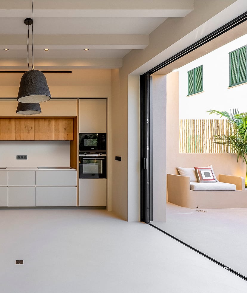 Modern kitchen with white and oak cabinetry, micro-cement floors, and sliding glass doors leading to a sun-drenched terrace.