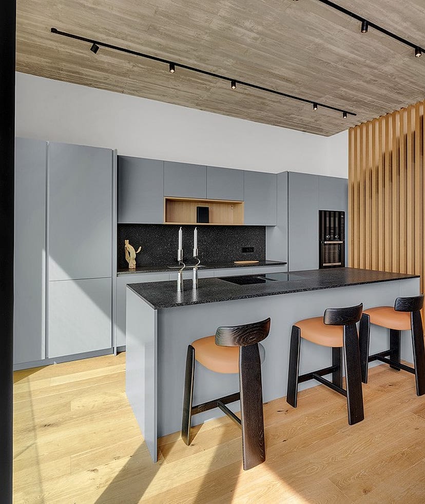 Modern open-plan kitchen featuring a gray island, oak wood slat room divider, light wood flooring, and track lighting.