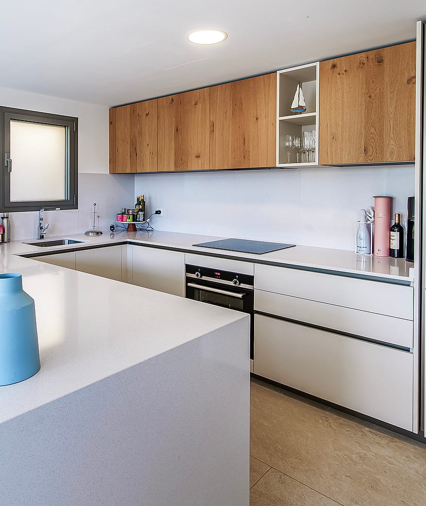 Modern U-shaped kitchen with white stone countertops, wood-veneer upper cabinets, and integrated appliances.