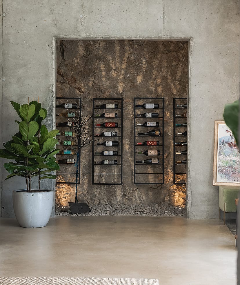 Minimalist wine storage area featuring black metal racks against an exposed rock wall and raw concrete finishes.