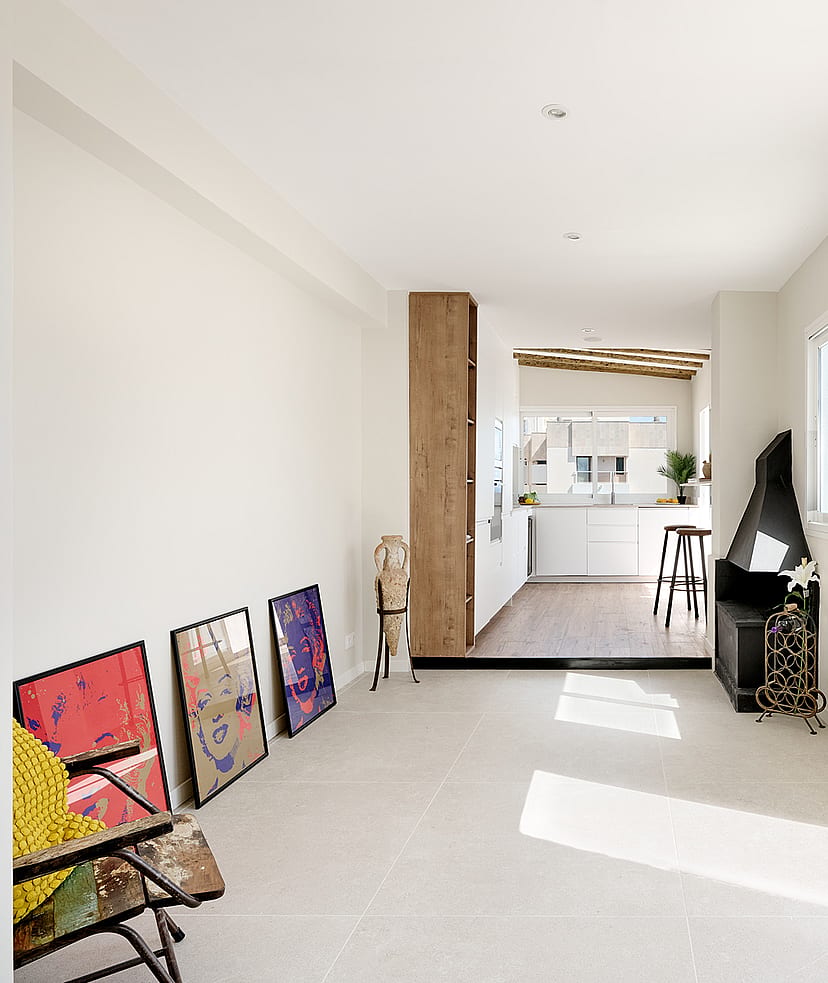 Bright living area with white walls, tile floors, and a corner fireplace, leading to an outdoor terrace with sea views.